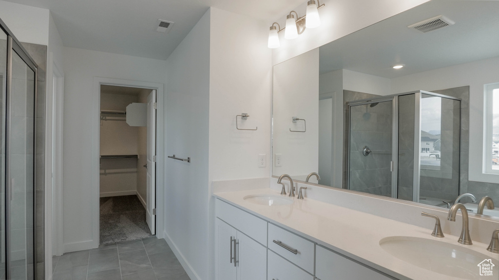 Bathroom featuring a walk in closet, double vanity, a stall shower, baseboards, and tile patterned flooring