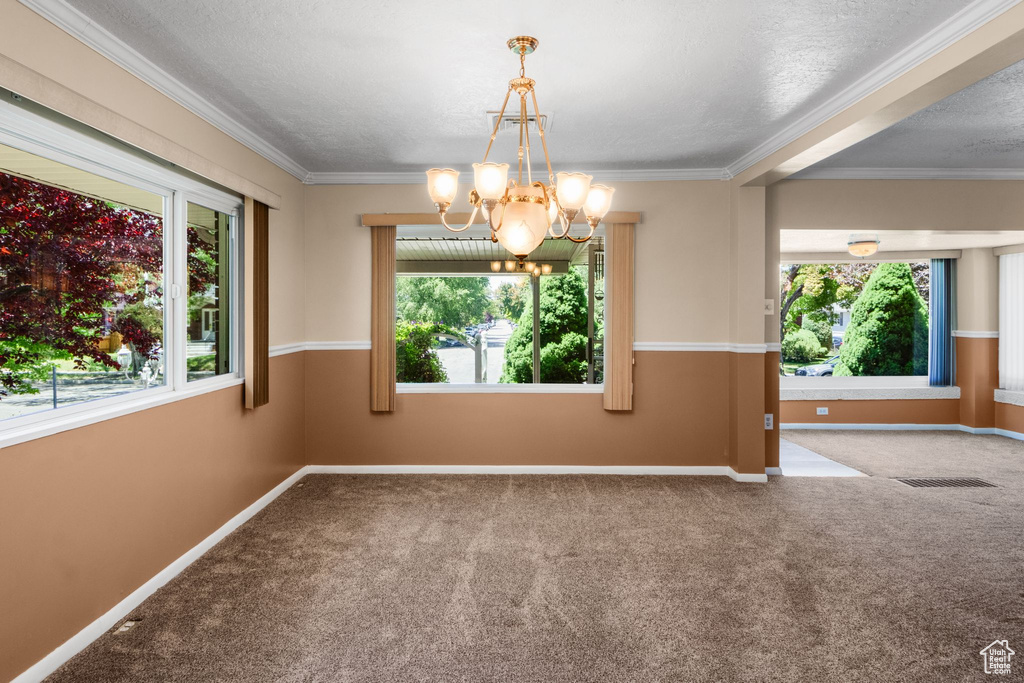 Carpeted empty room with plenty of natural light, a chandelier, baseboards, ornamental molding, and a textured ceiling