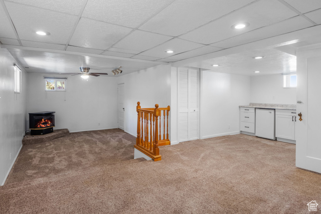 Below grade area featuring a wood stove, light carpet, recessed lighting, healthy amount of natural light, and a ceiling fan
