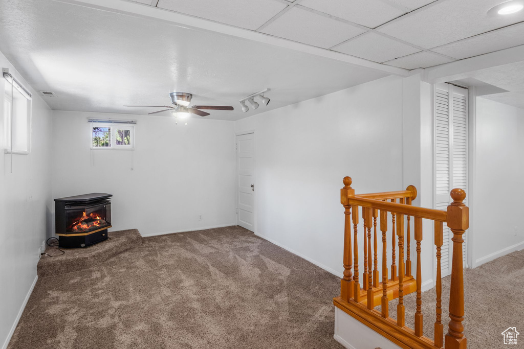 Unfurnished room with a wood stove, carpet flooring, a ceiling fan, rail lighting, and baseboards