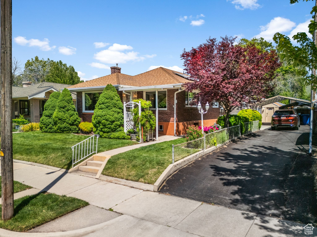 View of front of property with brick siding, a chimney, a carport, solar panels, and driveway