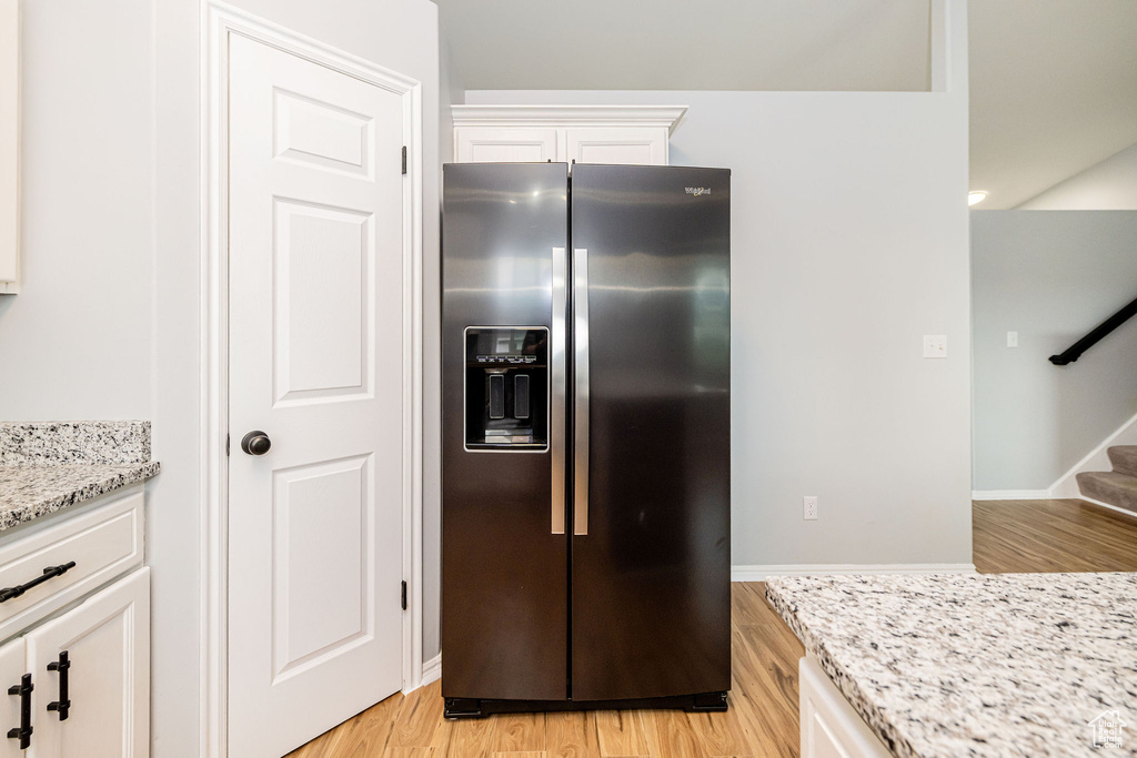Kitchen with stainless steel refrigerator with ice dispenser, light wood-type flooring, white cabinets, and light stone countertops