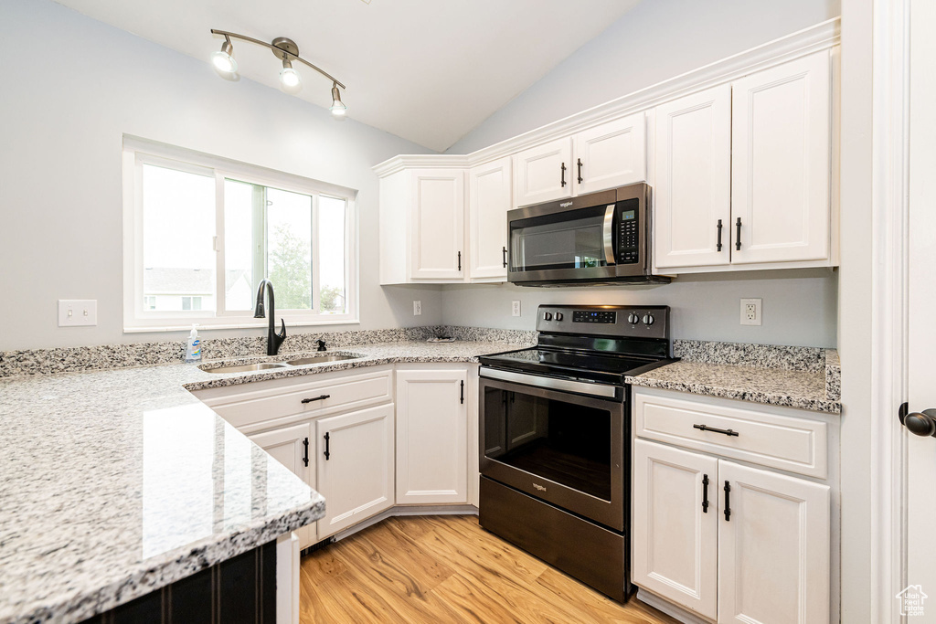 Kitchen featuring appliances with stainless steel finishes, a sink, white cabinets, light wood-style floors, and lofted ceiling