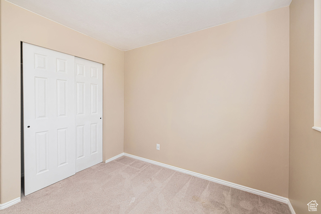 Unfurnished bedroom with light carpet, baseboards, and a closet