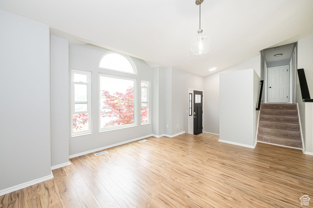 Unfurnished room with light wood finished floors, stairway, lofted ceiling, and baseboards