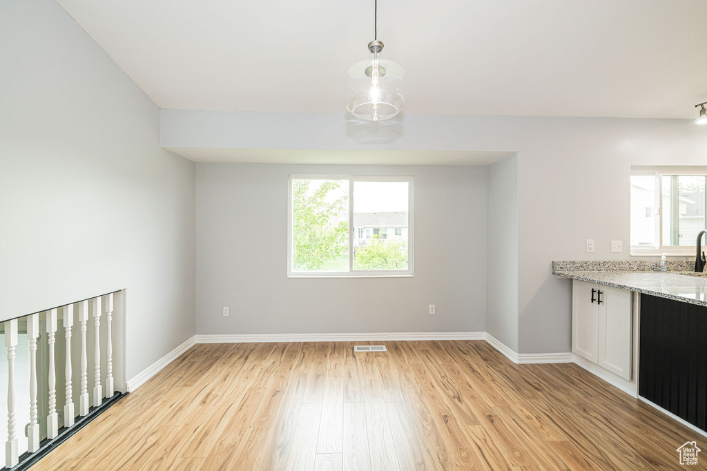 Unfurnished dining area with healthy amount of natural light, light wood-style floors, and baseboards