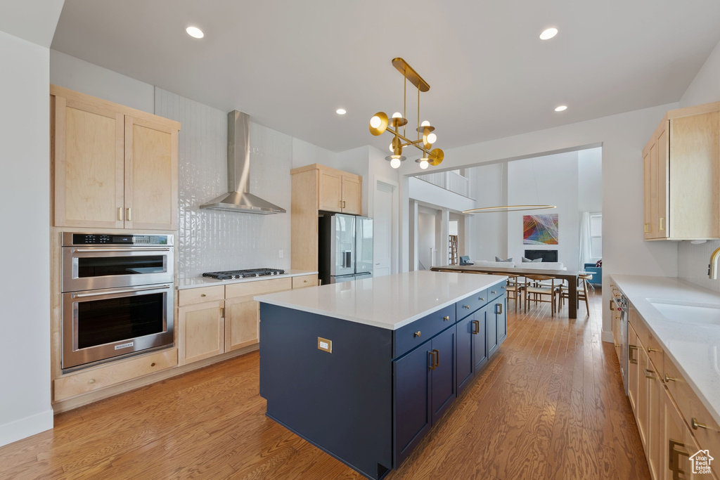 Kitchen with light brown cabinets, stainless steel appliances, wall chimney exhaust hood, light wood finished floors, and a sink