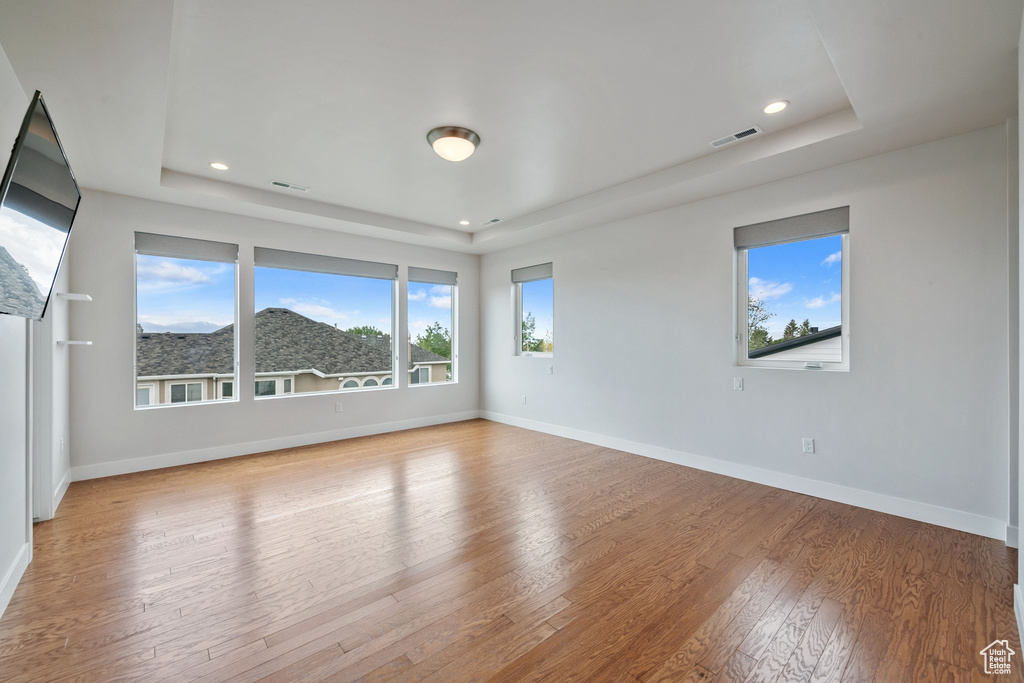 Unfurnished room featuring a tray ceiling, light wood finished floors, baseboards, and recessed lighting