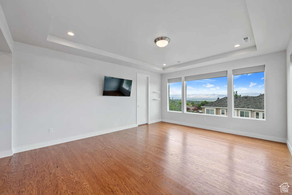 Unfurnished living room with a tray ceiling, light wood-style floors, baseboards, and recessed lighting