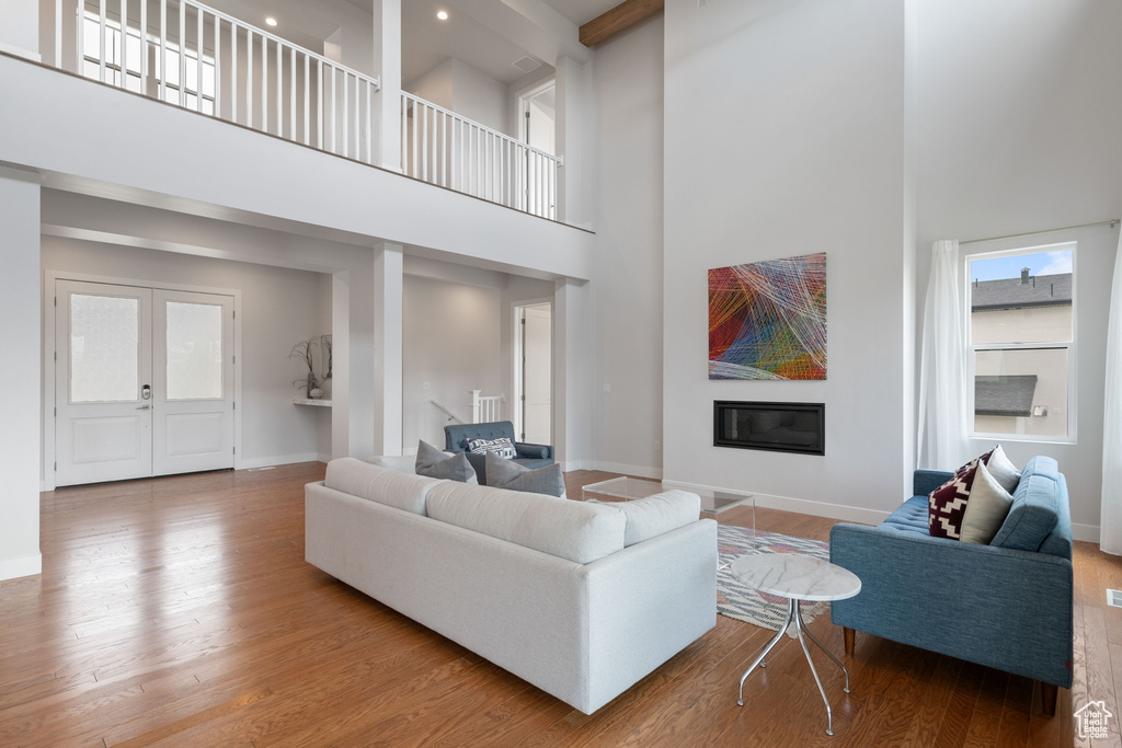 Living area featuring a towering ceiling, wood finished floors, baseboards, a glass covered fireplace, and recessed lighting