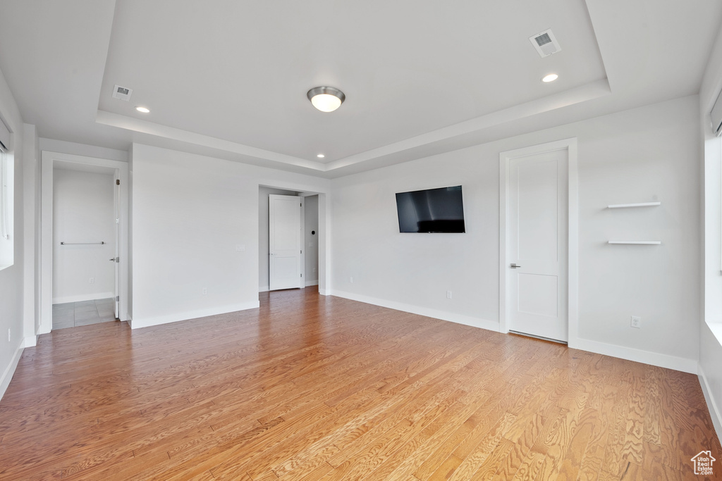 Unfurnished living room featuring a tray ceiling, light wood-style flooring, recessed lighting, and baseboards
