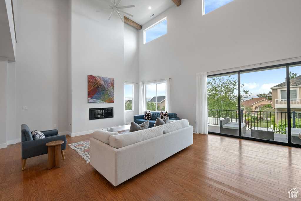 Living area featuring a towering ceiling, wood finished floors, ceiling fan, baseboards, and beamed ceiling