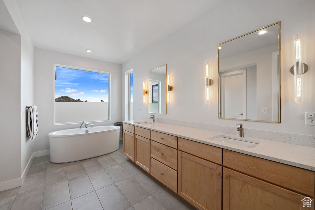 Bathroom with double vanity, a freestanding tub, tile patterned floors, recessed lighting, and baseboards