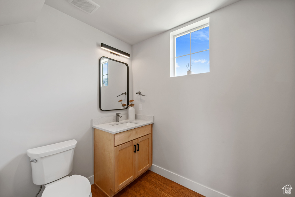 Bathroom with toilet, vanity, wood finished floors, and baseboards