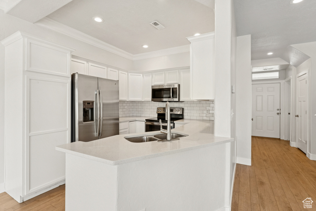 Kitchen with stainless steel appliances, light countertops, white cabinetry, a peninsula, and recessed lighting