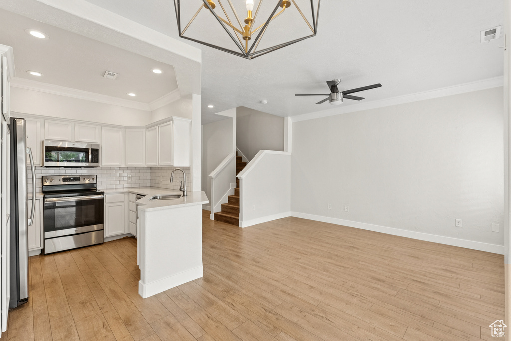 Kitchen with stainless steel appliances, open floor plan, crown molding, white cabinetry, and decorative backsplash