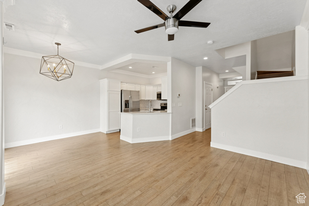 Unfurnished living room with a chandelier, ceiling fan, light wood-type flooring, stairs, and recessed lighting