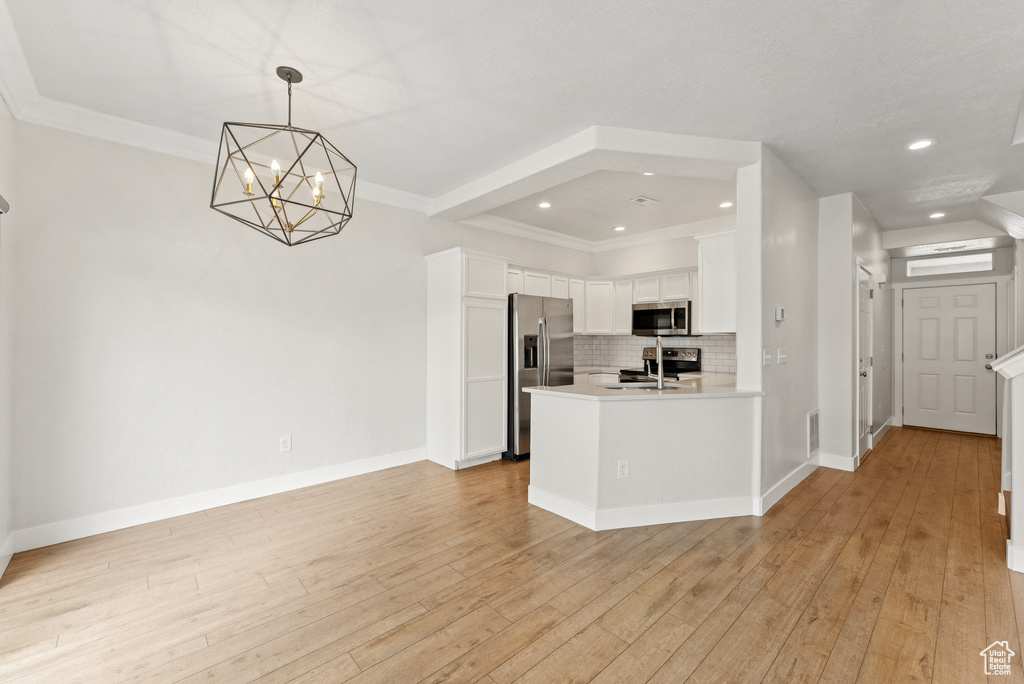 Kitchen with stainless steel appliances, backsplash, white cabinets, light countertops, and a chandelier