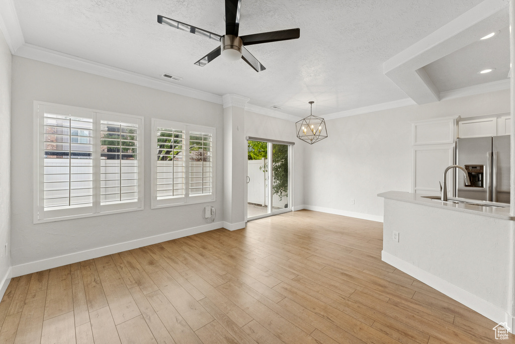 Unfurnished living room with a chandelier, ceiling fan, light wood-type flooring, ornamental molding, and a textured ceiling