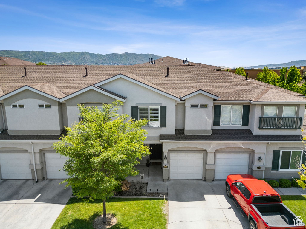 Townhome / multi-family property featuring stucco siding, an attached garage, driveway, a mountain view, and roof with shingles