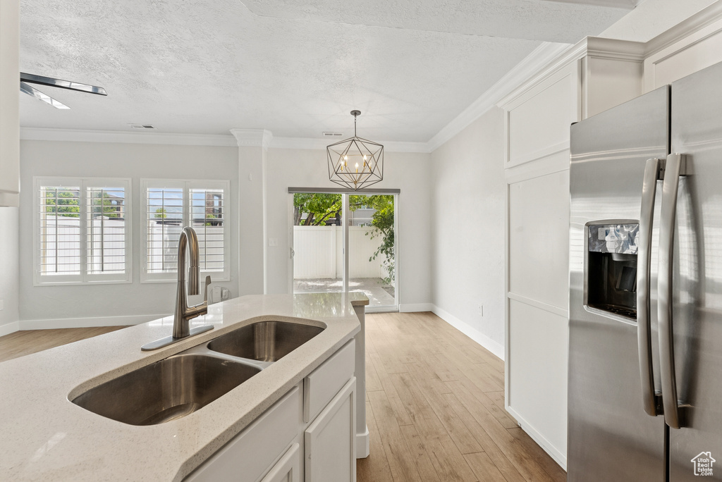 Kitchen with stainless steel fridge, light wood-type flooring, light stone countertops, healthy amount of natural light, and a textured ceiling