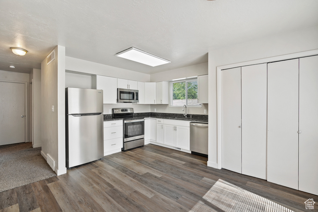 Kitchen with stainless steel appliances, dark countertops, dark wood-style flooring, a sink, and white cabinetry
