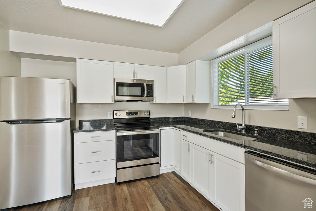 Kitchen with stainless steel appliances, a sink, dark stone countertops, white cabinetry, and dark wood-type flooring