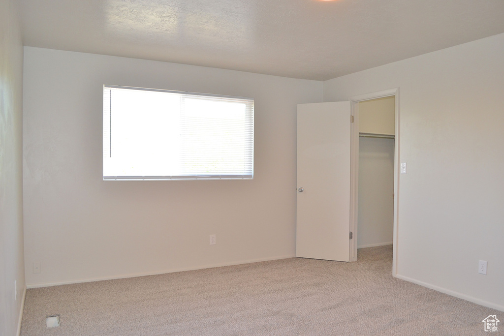 Unfurnished bedroom with a walk in closet, light colored carpet, and a closet