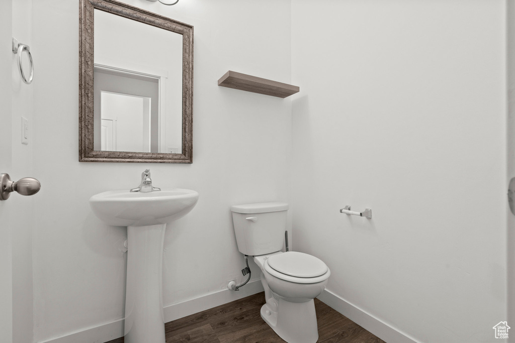 Half bathroom with toilet, wood finished floors, baseboards, and a sink