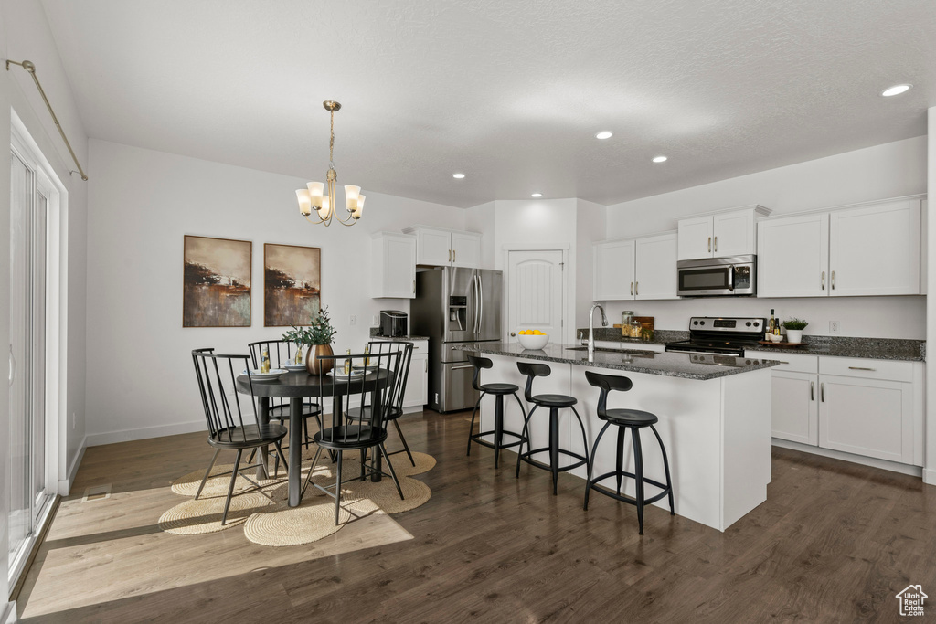 Kitchen featuring stainless steel appliances, dark wood-style flooring, a kitchen bar, a chandelier, and a sink