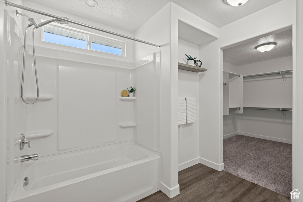 Full bathroom with a textured ceiling, washtub / shower combination, a walk in closet, wood finished floors, and baseboards