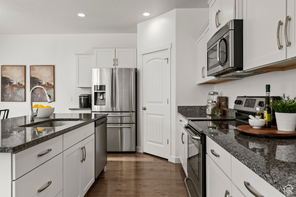 Kitchen featuring stainless steel appliances, a sink, dark stone counters, white cabinetry, and dark wood-type flooring
