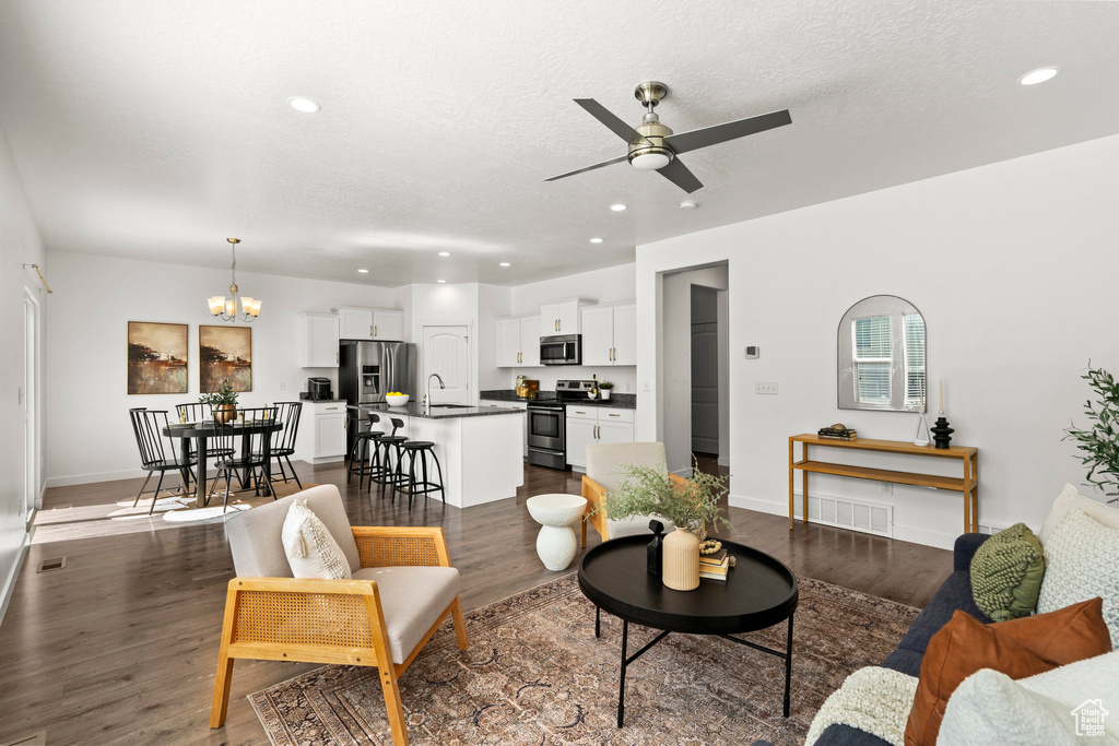 Living area with a ceiling fan, a chandelier, recessed lighting, dark wood-style floors, and a textured ceiling