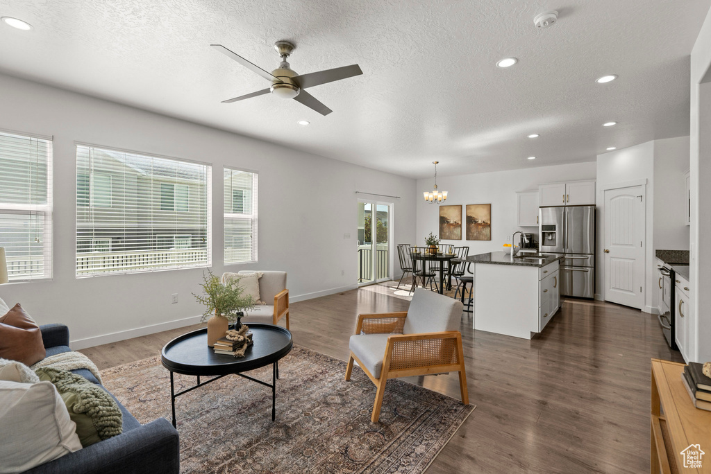 Living room with a chandelier, a ceiling fan, a textured ceiling, recessed lighting, and dark wood-type flooring