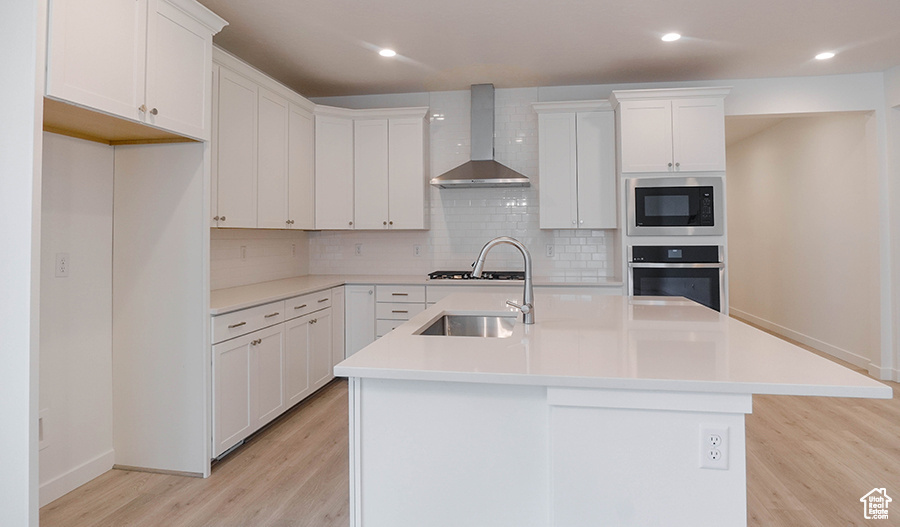 Kitchen with wall chimney range hood, oven, built in microwave, light wood-style floors, and decorative backsplash