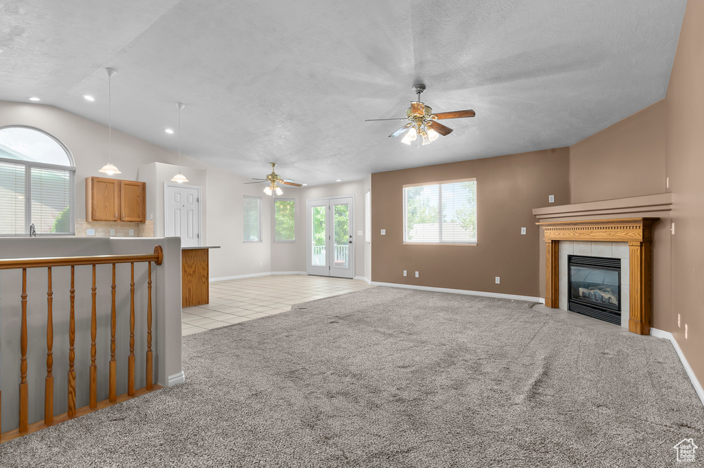 Unfurnished living room with ceiling fan, light colored carpet, a tiled fireplace, light tile patterned floors, and baseboards