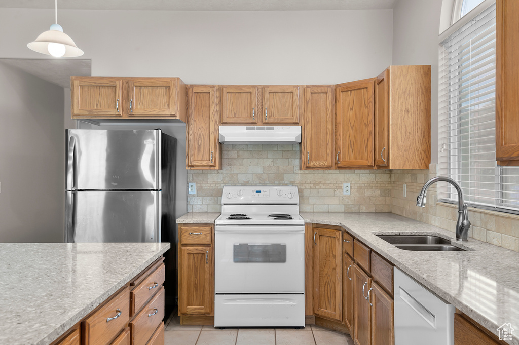 Kitchen featuring white appliances, a sink, under cabinet range hood, backsplash, and light stone countertops