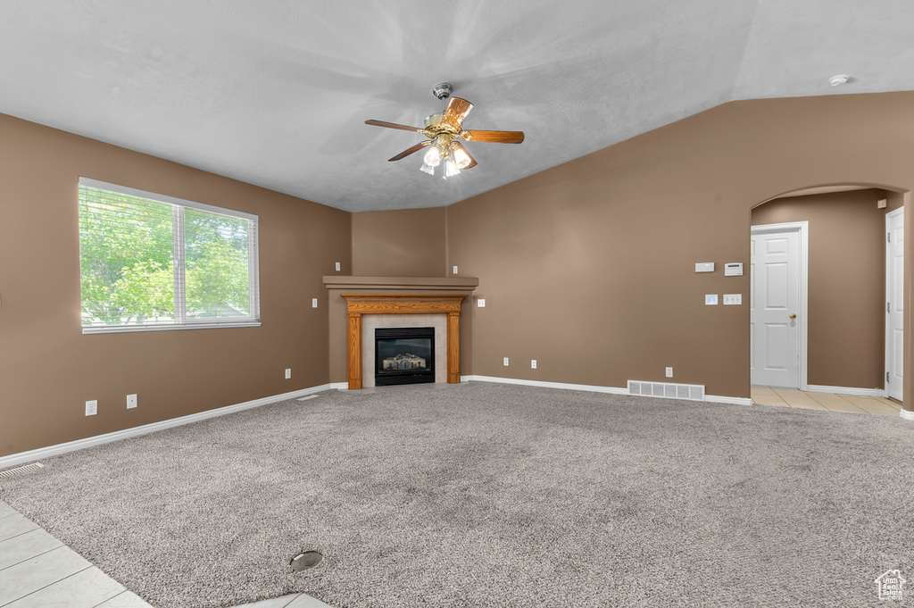 Unfurnished living room with arched walkways, ceiling fan, a fireplace, vaulted ceiling, and baseboards