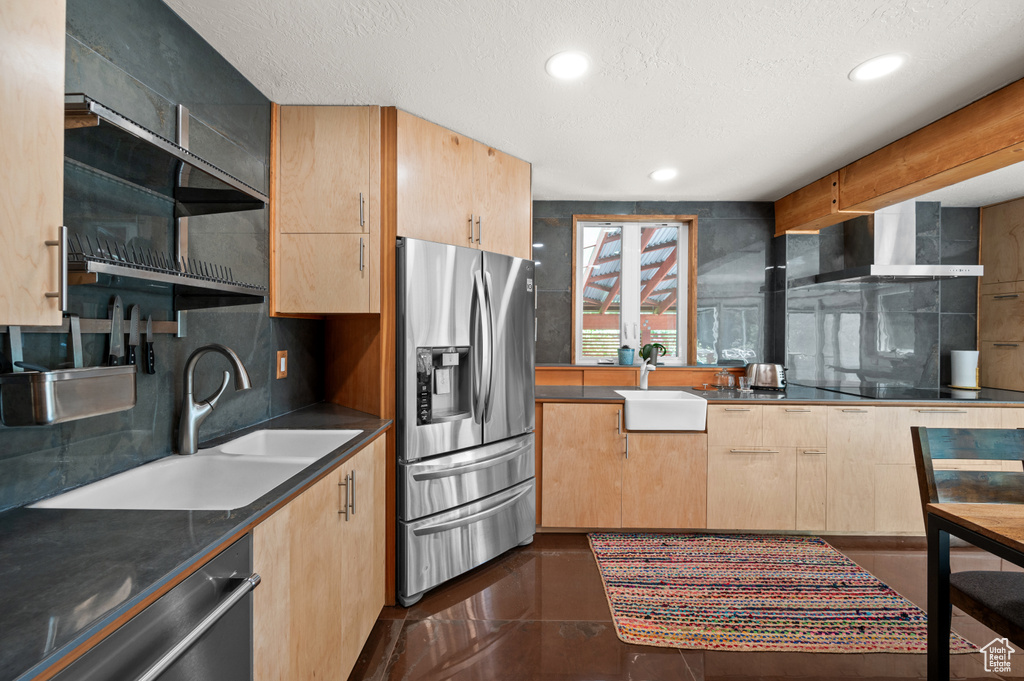 Kitchen featuring appliances with stainless steel finishes, wall chimney exhaust hood, a sink, light brown cabinetry, and a textured ceiling