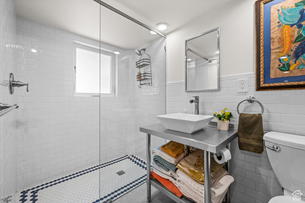 Bathroom with a sink, toilet, tiled shower, wainscoting, and tile walls