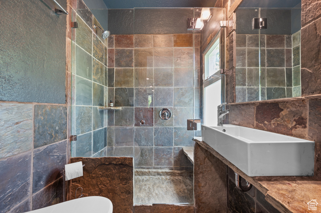 Full bath with tiled shower, toilet, tile walls, and a sink