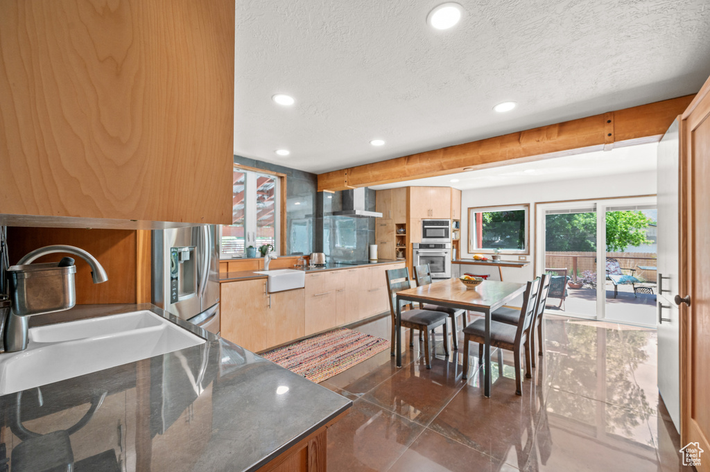 Kitchen featuring appliances with stainless steel finishes, a sink, a textured ceiling, recessed lighting, and wall chimney range hood