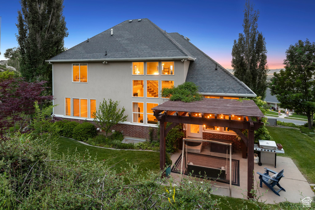 Back of property featuring stucco siding, a patio area, a lawn, and roof with shingles