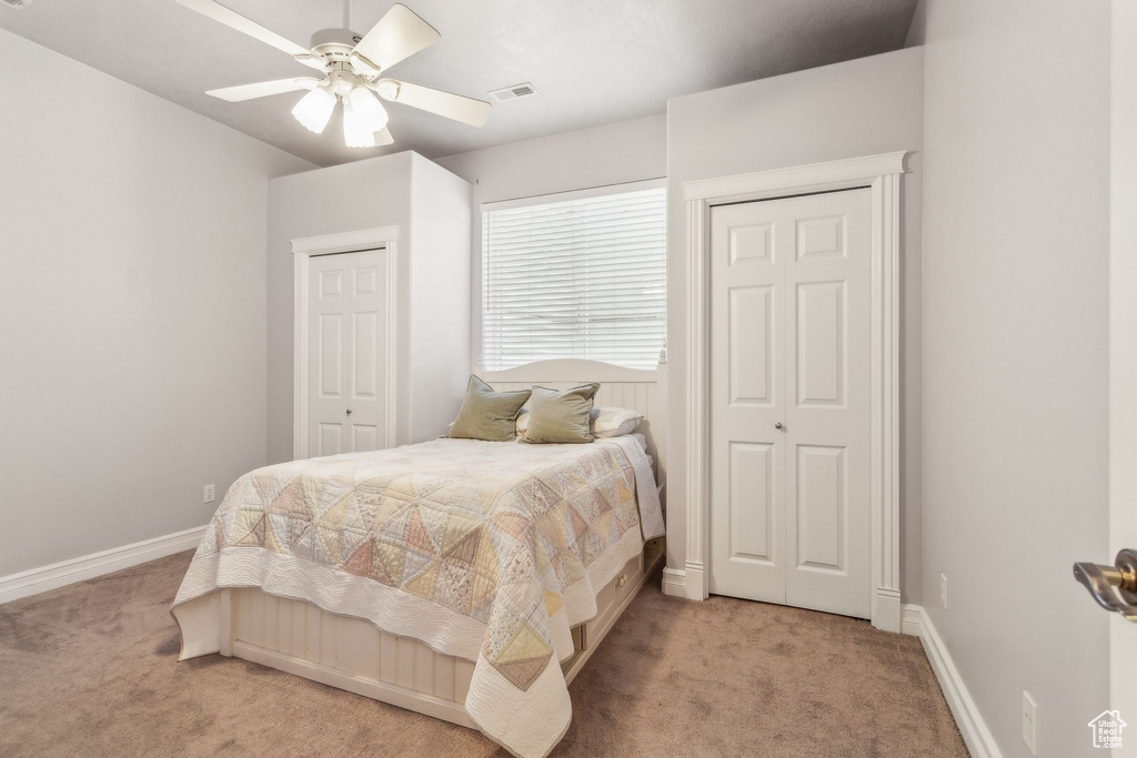 Bedroom featuring light carpet, two closets, baseboards, and ceiling fan