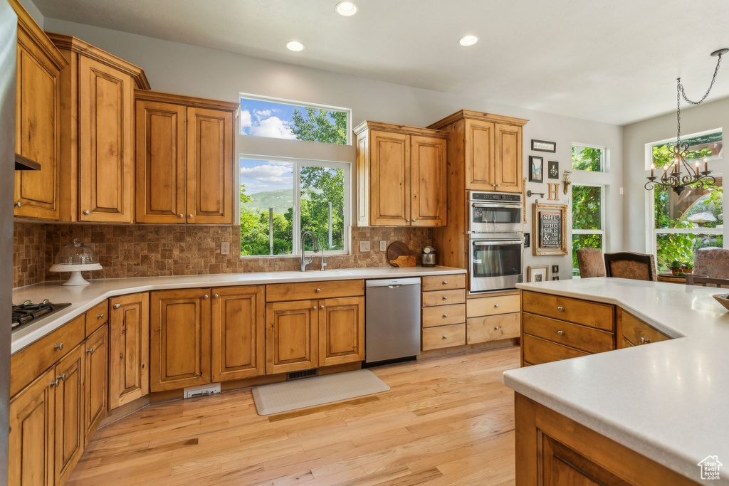 Kitchen featuring appliances with stainless steel finishes, tasteful backsplash, light wood-style floors, light countertops, and recessed lighting