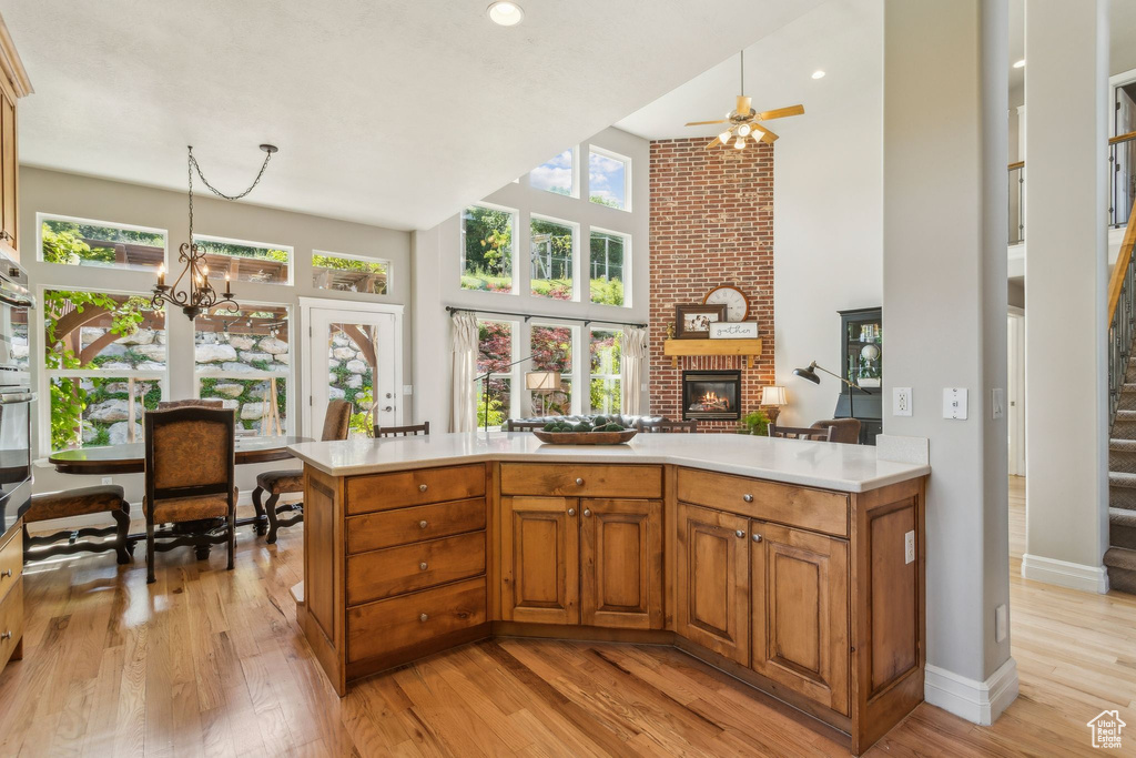 Kitchen featuring a high ceiling, a fireplace, light countertops, light wood-type flooring, and a ceiling fan