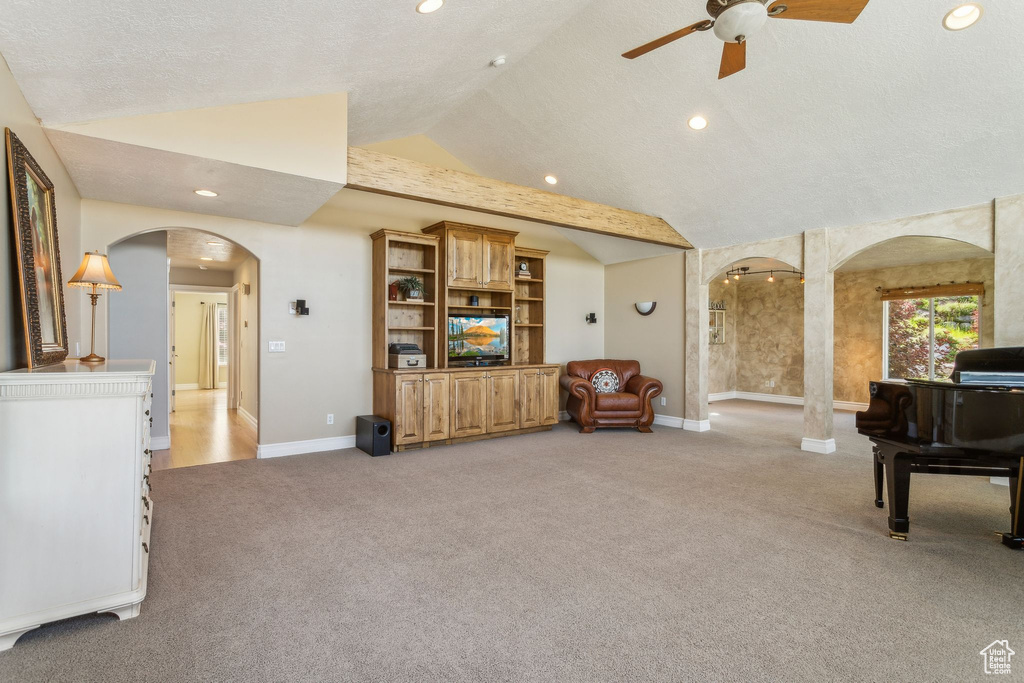 Living area with arched walkways, light colored carpet, vaulted ceiling, a ceiling fan, and baseboards