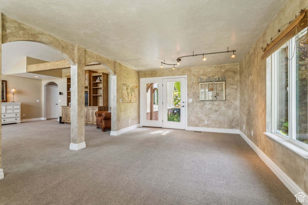 Unfurnished living room with arched walkways, baseboards, carpet flooring, and a textured ceiling