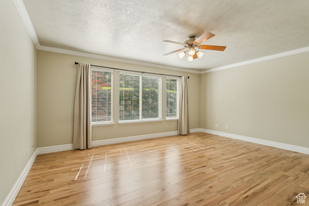 Empty room with a textured ceiling, a ceiling fan, light wood finished floors, crown molding, and baseboards