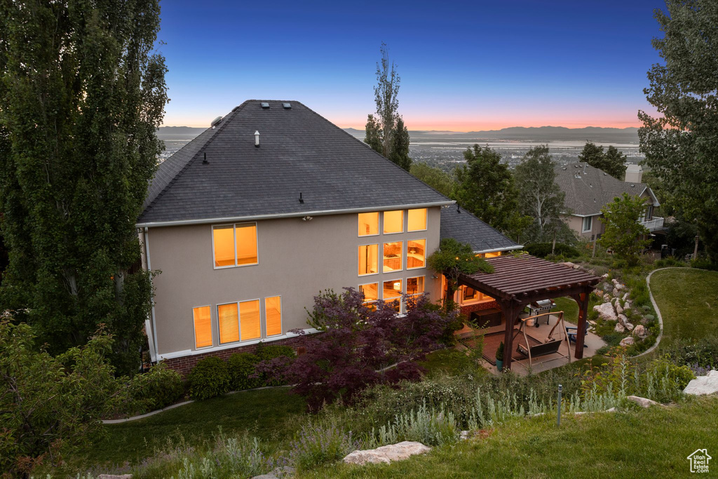 Back of property at dusk with a pergola, stucco siding, a patio, and roof with shingles